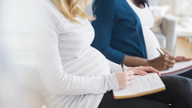 A close up of a sitting pregnant woman wearing a striped white top